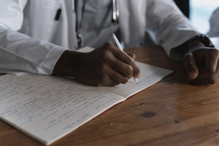 Doctor writing notes in a notebook at a wooden desk