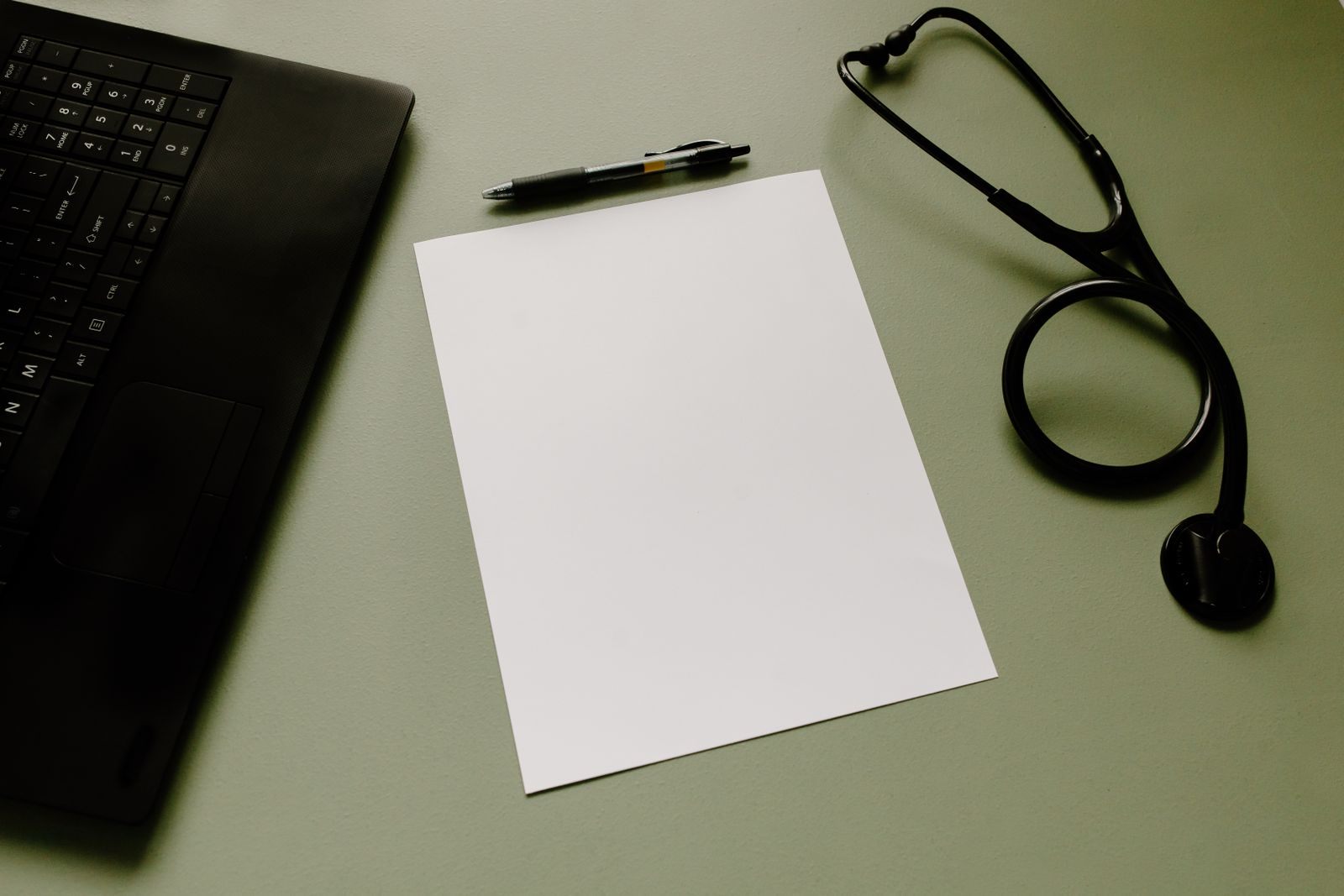 Laptop, blank paper, pen and stethoscope on a desk